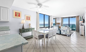 A modern hotel room with a dining area, a balcony with a view of the sea, and a ceiling fan.