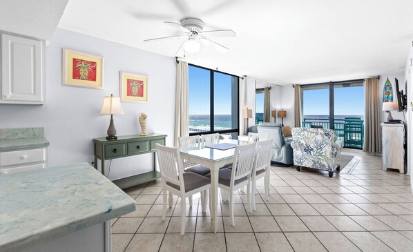 A modern hotel room with a dining area, a balcony with a view of the sea, and a ceiling fan. - SunDestin 2BR Condo Sleeps 6 With Balcony Dining and Laundry - Unit 0501 (Destin)