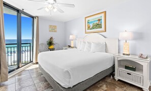 A hotel room with a large bed, two bedside lamps, a ceiling fan, a painting, and a view of the beach. - SunDestin 2BR Condo Sleeps 6 With Balcony Dining and Laundry - Unit 0501 (Destin)