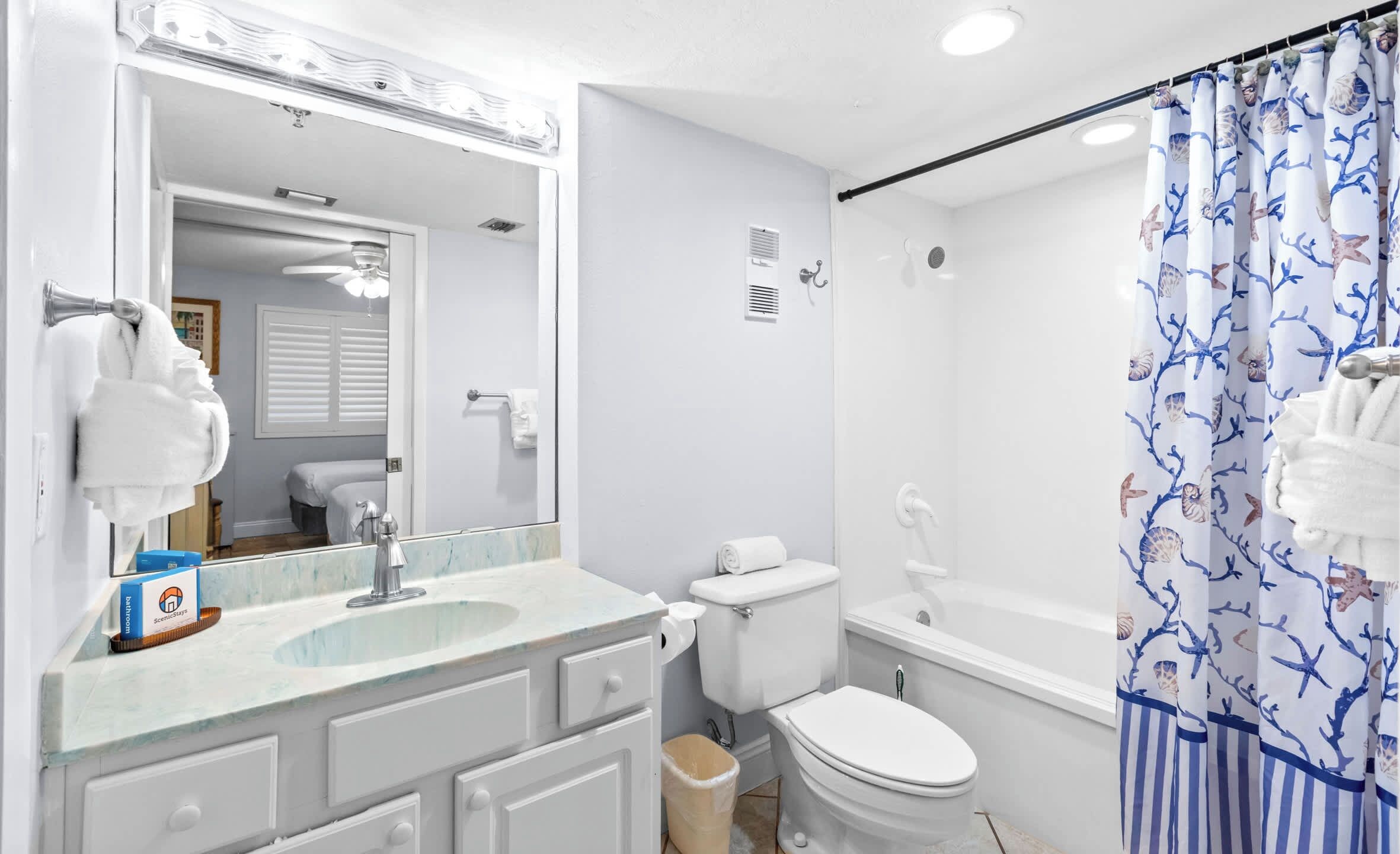 Un baño con lavamanos blanco, inodoro y cortina de ducha con motivos marinos.