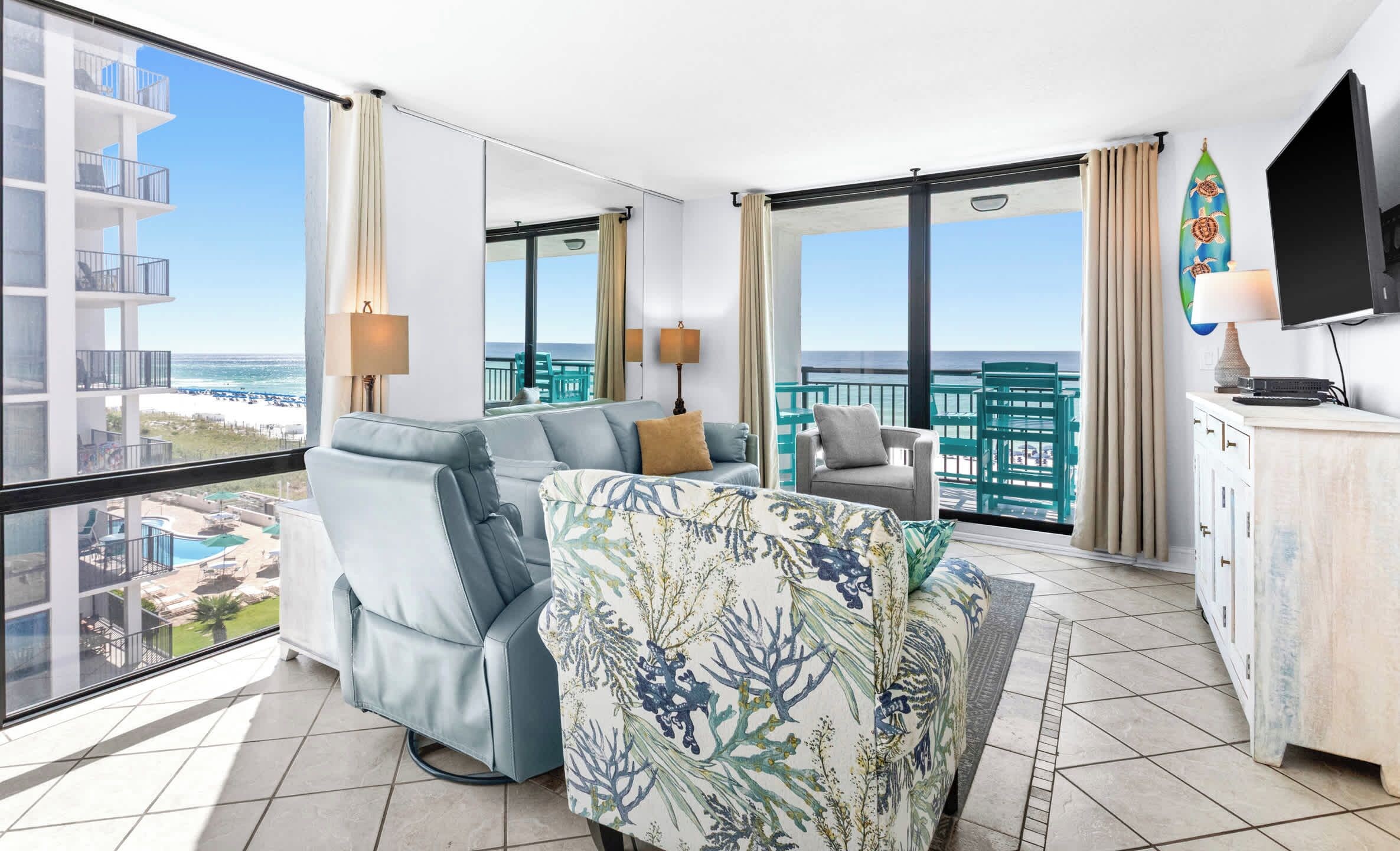 Quarto de hotel moderno com varanda, sofá, poltrona, televisão e vista para a praia.
