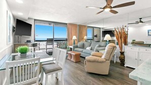 A spacious living area with a balcony, a sofa, a chair, a dining table, and a kitchen area. - 1BR Condo Sleeps 6 With Gulf Views and In-Unit Laundry - SunDestin Unit 0308 (Destin)