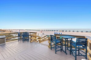 Une terrasse en bois avec des tables et des chaises donnant sur une plage.