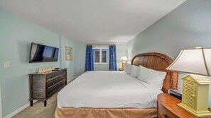 Une chambre à coucher avec un grand lit, une commode, un téléviseur et une fenêtre avec des rideaux.