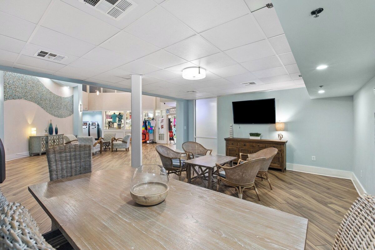 A spacious living area with a wooden dining table, wicker chairs, and a flat-screen TV mounted on the wall.