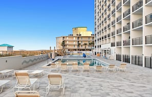 A rooftop pool area with lounge chairs, a pool, and a building with balconies in the background. - SunDestin Resort Unit 0212 (Destin)