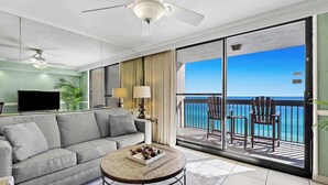 Ein modernes Wohnzimmer mit einem grauen Sofa, einem Holztisch und einem Flachbildfernseher. Ein Balkon bietet Blick aufs Meer.