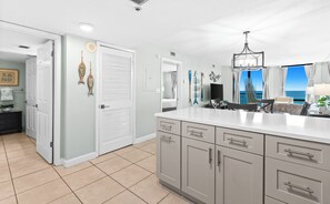 A modern kitchen with a large island, white cabinetry, and a view of the ocean through the windows. - 1BR Beachfront Living with Unforgettable Gulf Scenery (Destin)