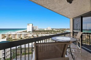 A balcony with a view of the ocean and cityscape, a round table, and wicker chairs.
