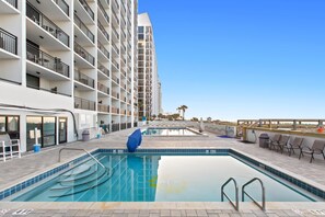 A swimming pool with a view of a high-rise building, outdoor seating, and a clear sky.