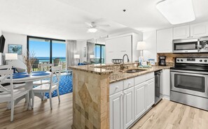 A modern kitchen with a central island, stainless steel appliances, and a view of the ocean. - SunDestin Resort Unit 0204 (Destin)