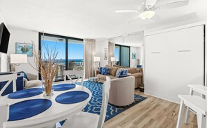 A modern living room with a dining area, large windows, and a view of the ocean. - SunDestin Resort Unit 0204 (Destin)