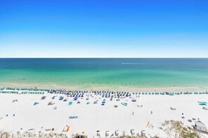 Une plage bordée de rangées de chaises longues et de parasols bleus et blancs, un ciel bleu dégagé et l’océan en toile de fond.