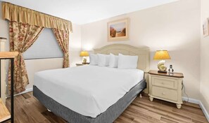 Une chambre à coucher bien rangée, avec un grand lit, deux tables de chevet avec des lampes, une fenêtre avec des rideaux et un tableau encadré au mur.