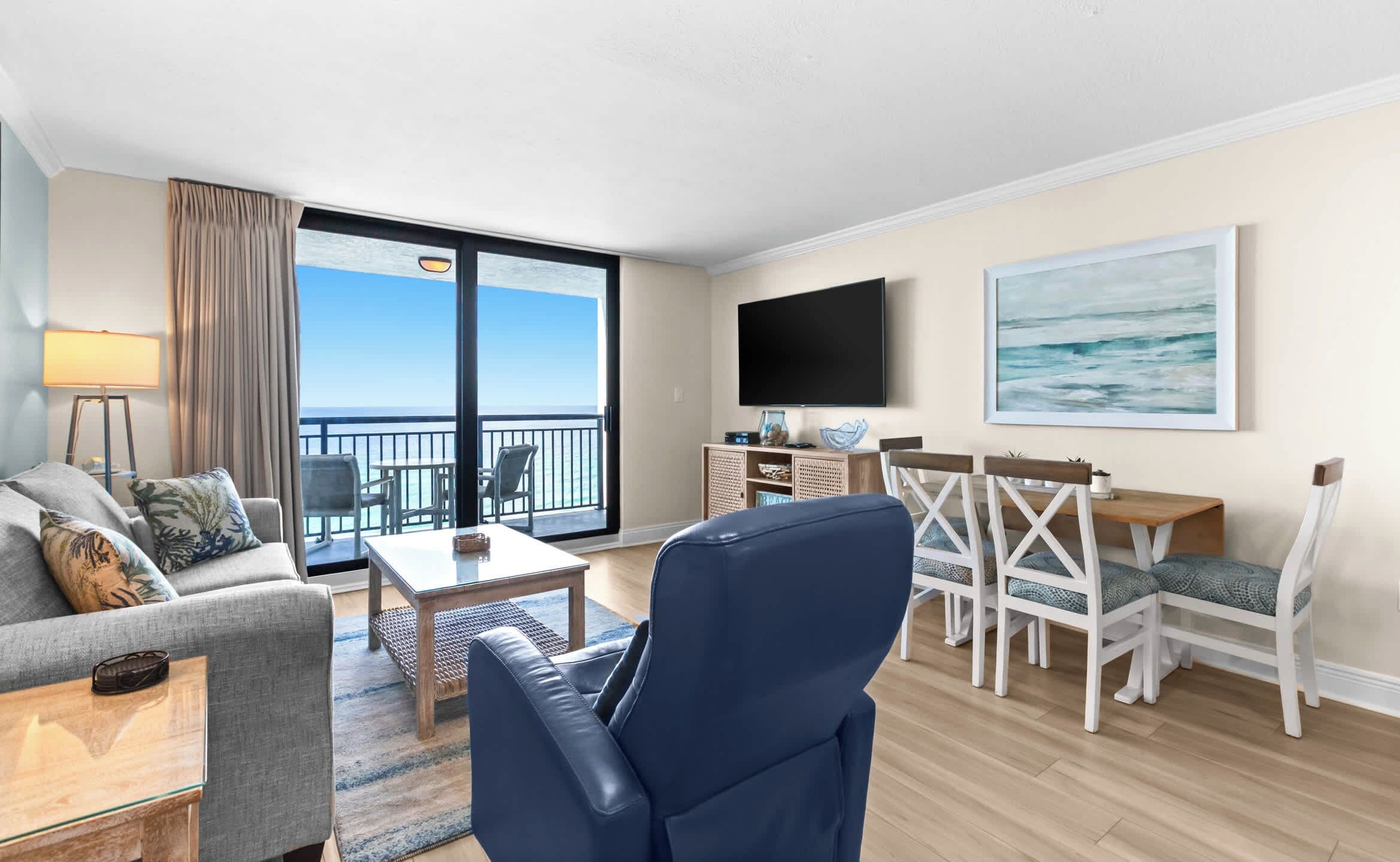 Une chambre d’hôtel avec un balcon, un téléviseur à écran plat, un coin repas avec des chaises blanches et un canapé.
