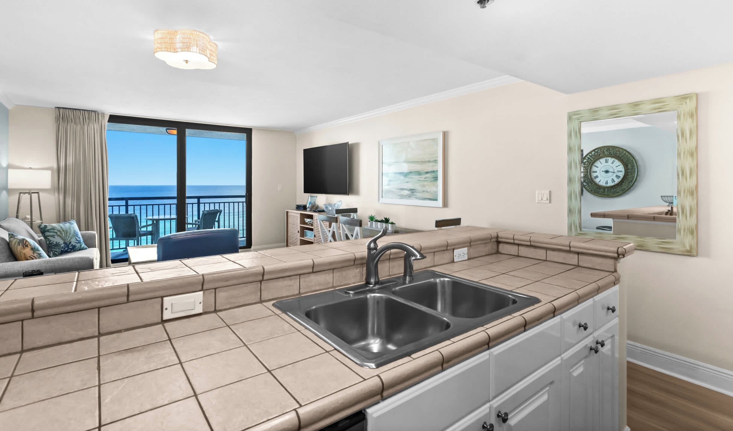 A modern kitchen with a large window overlooking the ocean, a built-in sink, and a flat-screen TV mounted on the wall.