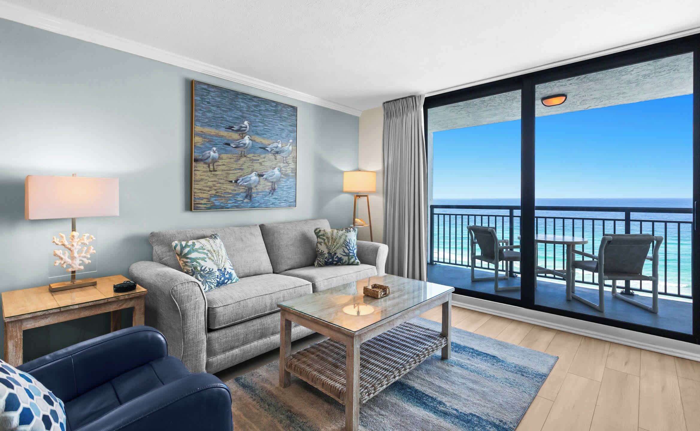 Une chambre d’hôtel moderne avec un balcon, un canapé, une table basse et un tableau représentant des mouettes.