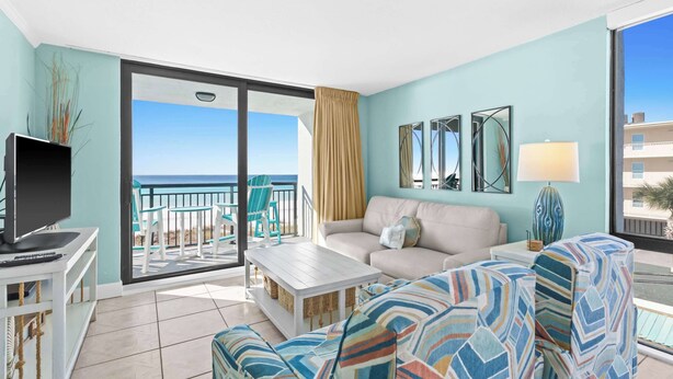 Un soggiorno con divano, tavolino e televisore su un mobile. È presente un balcone con vista sull'oceano.