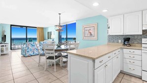 Una cucina moderna con mobili bianchi e una grande isola, una zona pranzo con vista sull'oceano e un balcone con vista sul mare.