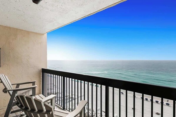 A balcony with two Adirondack chairs overlooking a beach with umbrellas. - SunDestin Resort Unit 1207 (Destin)