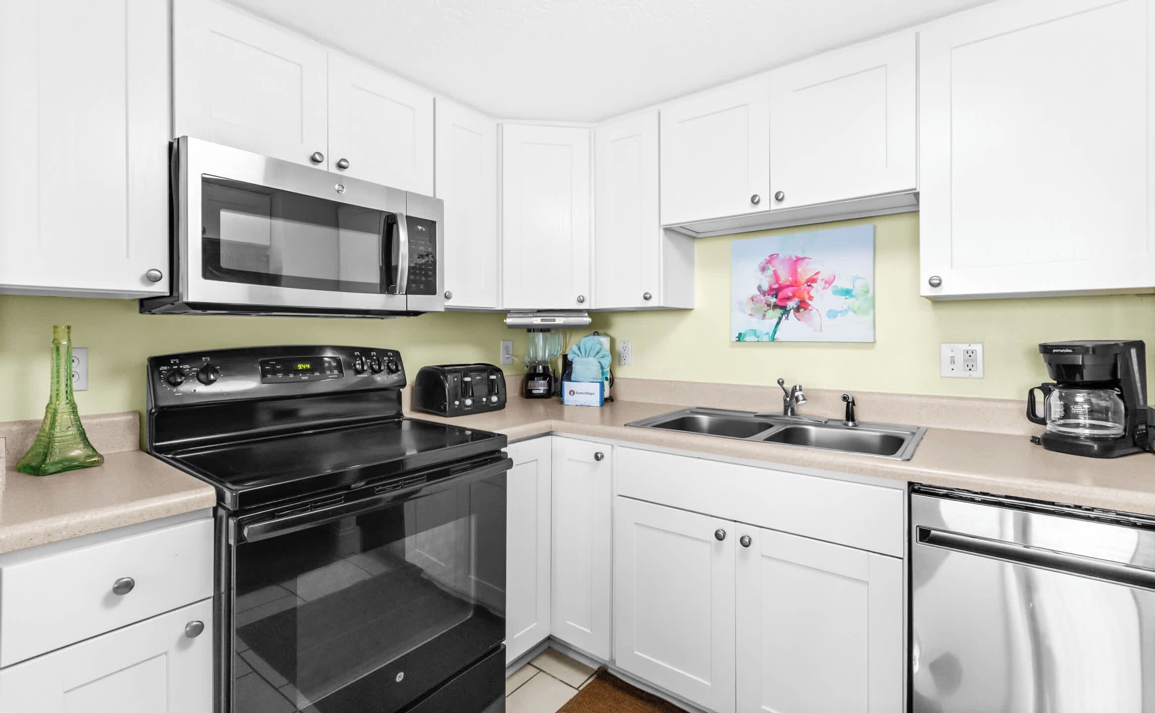A modern kitchen with white cabinets, a black stove, a microwave, a coffee maker, and a sink.