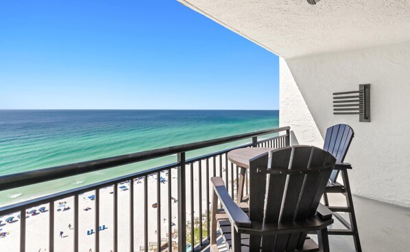 A balcony with a view of the ocean, a table, two chairs, and a railing.