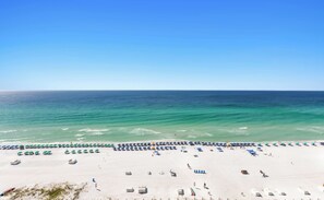 A beach with rows of umbrellas and sun loungers, a sandy shore, and the ocean in the background.