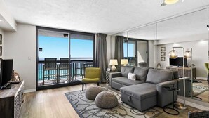 A modern living room with a grey sectional sofa, a yellow armchair, and a large sliding glass door leading to a balcony. - SunDestin Resort Unit 1402 (Destin)