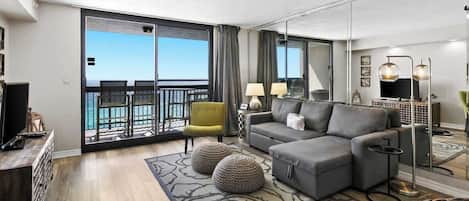 A modern living room with a grey sectional sofa, a yellow armchair, and a large sliding glass door leading to a balcony.