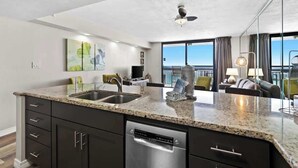 A modern kitchen with granite countertops, a dishwasher, and a large window offering a view of the city. - SunDestin Resort Unit 1402 (Destin)