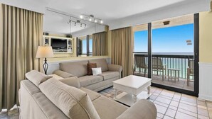 A hotel room with a large sofa, a coffee table, a TV, and a balcony with a view of the ocean. - Spacious 2BR Destin Condo With Gulf Views and Private Balcony (Destin)