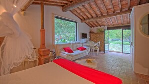 A bedroom with a large bed, a white sofa with red cushions, a wooden pillar, and a view of the garden through a sliding door. - Villa Ancora - House with private pool (Cercina)