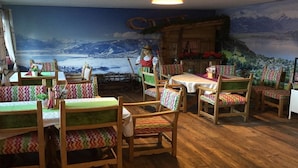 A restaurant with wooden tables and chairs, a mural of a mountainous landscape, and a cozy interior.