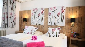 A hotel room with a large bed, floral wall art, two bedside tables with lamps, and a window with curtains.