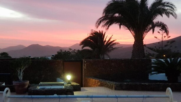 A swimming pool with a sunset view, a palm tree, and a stone wall. - Villa Lucky (Tías)