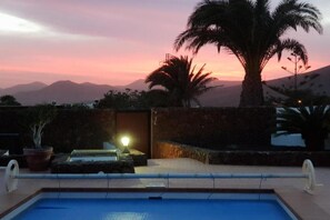 A swimming pool with a sunset view, a palm tree, and a stone wall. - Villa Lucky (Tías)