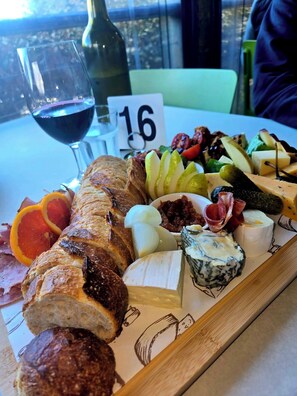 Un tagliere con diversi formaggi, salumi e frutta su un tavolo di legno, accompagnato da un bicchiere di vino rosso.