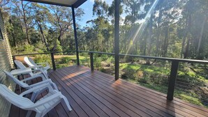 A wooden deck with white plastic chairs, overlooking a forested area. - A beautiful chalet in a secluded bush environment, only a short walk to town. (Denmark)