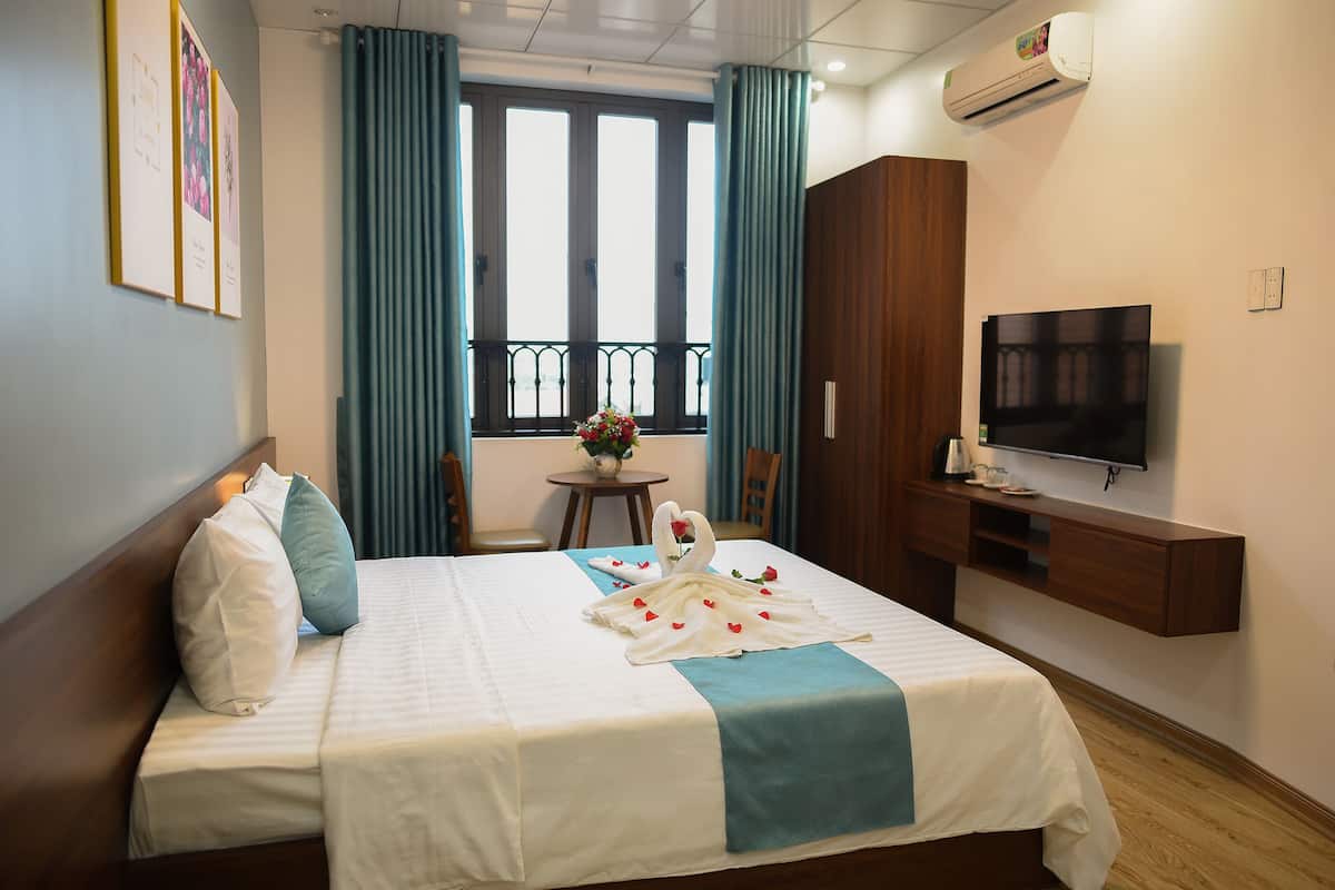 A hotel room with a bed, a TV, a desk, and a window with curtains.