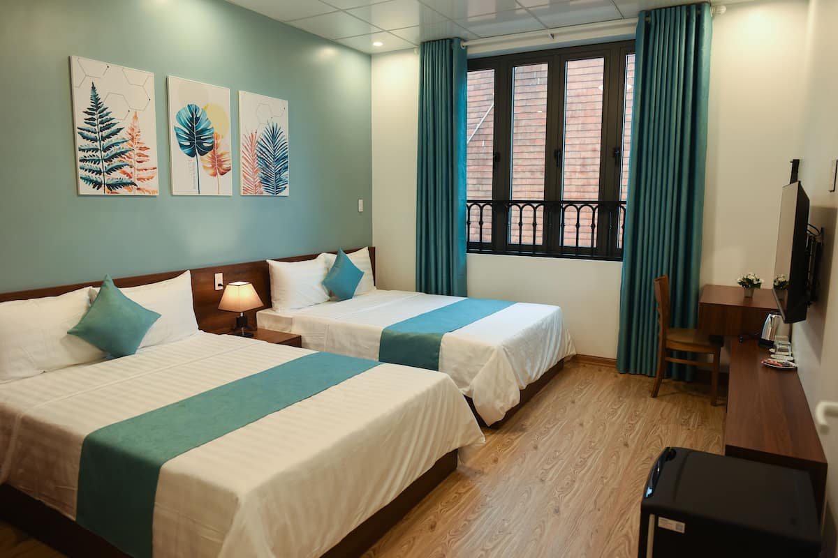 A hotel room with two beds, a desk, a chair, a TV, and a window with curtains.
