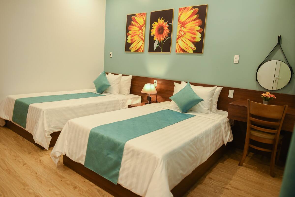 A hotel room with two beds, a wooden headboard, a round mirror, and a flower vase.