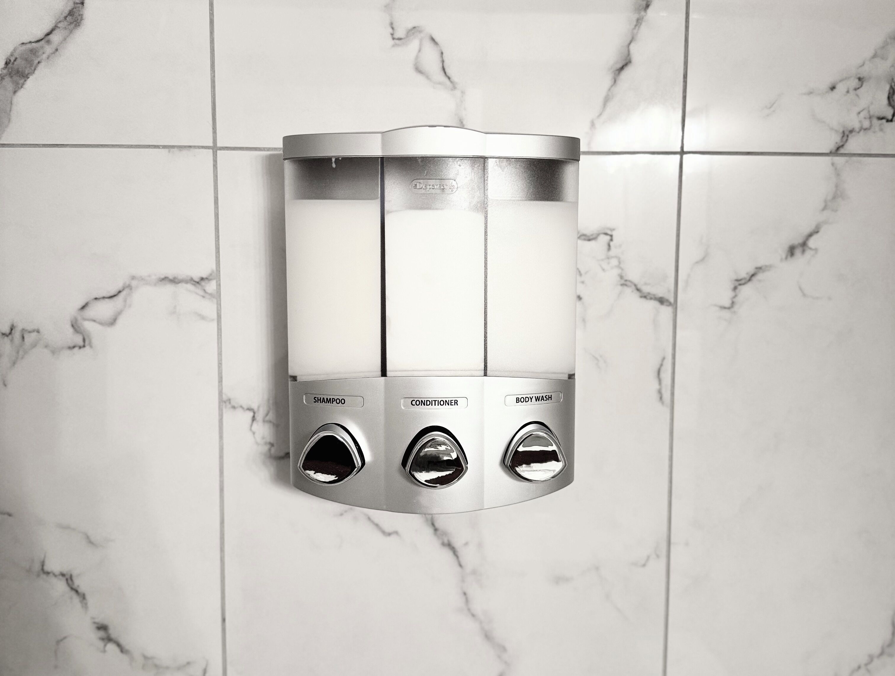 Une douche murale dotée de trois robinets de commande étiquetés « shampoing », « après-shampoing » et « gel douche ».