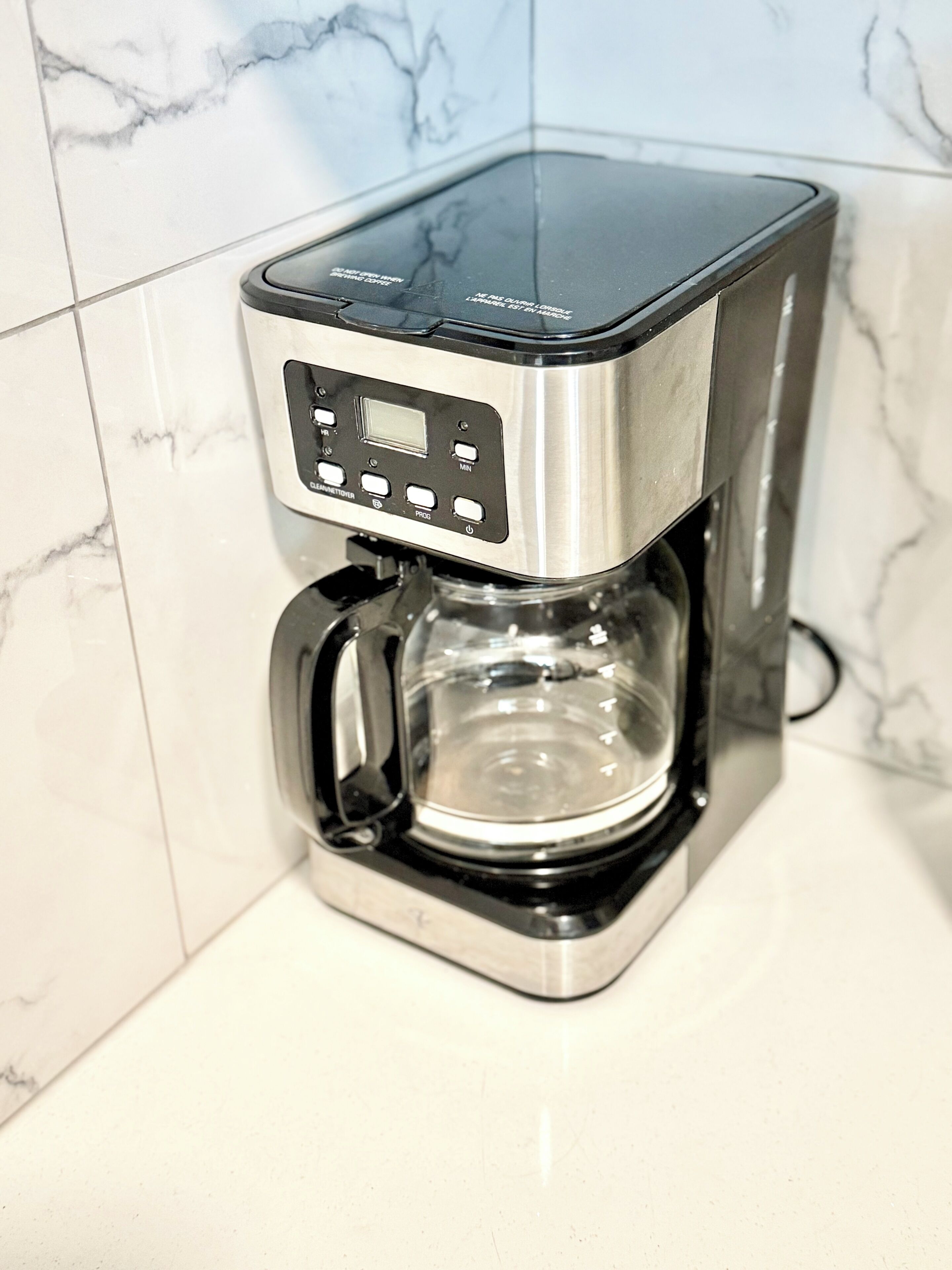 A coffee maker with a digital control panel, a transparent water reservoir, and a black drip tray.