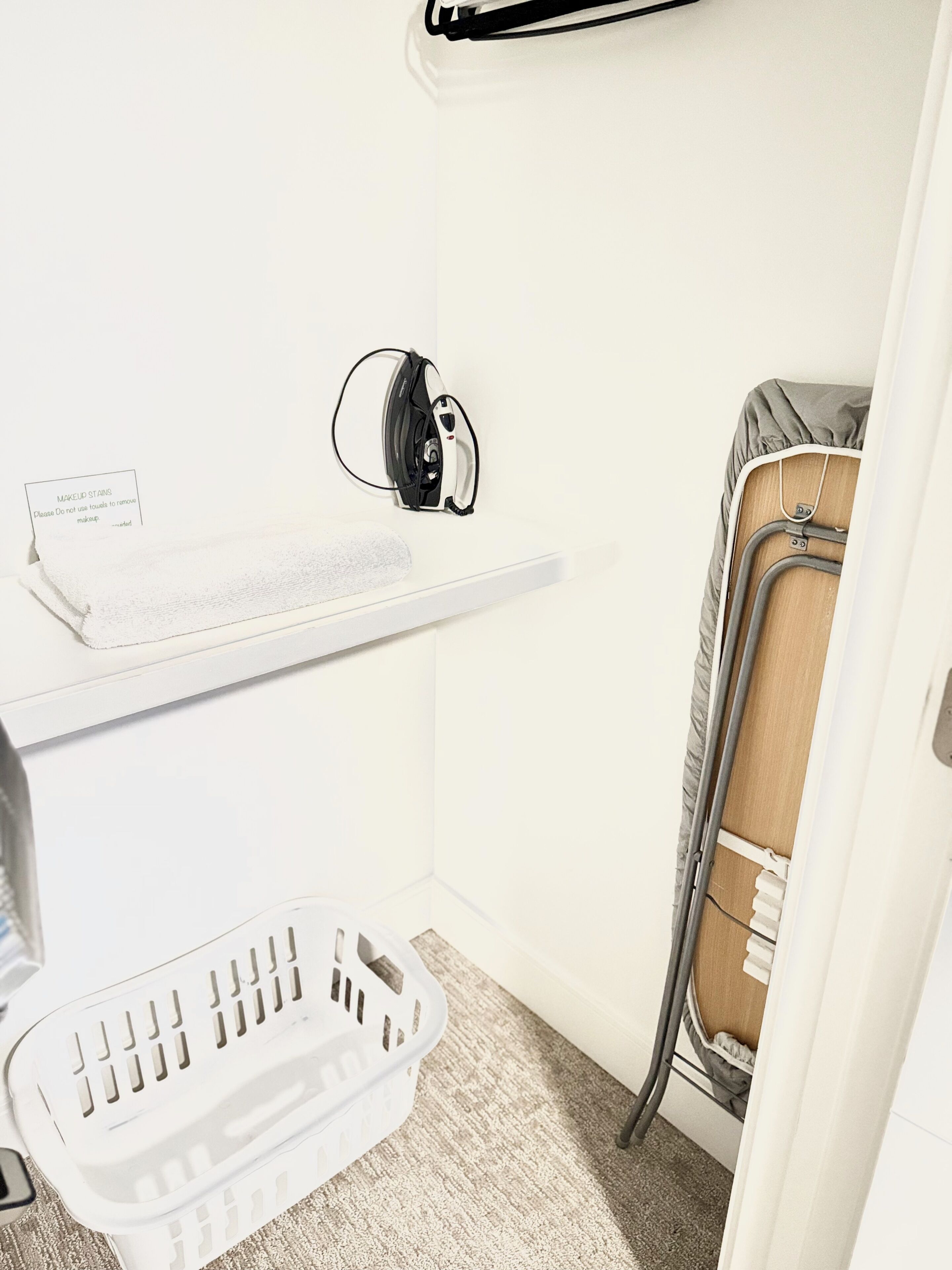 A small laundry area with a washing machine, a drying rack, and a shelf with a label.
