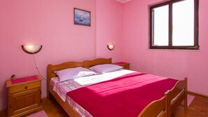 A pink-themed bedroom with a wooden bed, two bedside tables, a nightstand, a window, and a wall-mounted picture. - Apartments Neve (Dubrovnik)