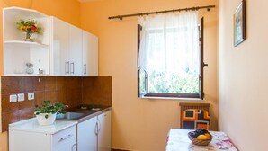 A compact kitchen with white cabinets, a countertop, and a window with a curtain. - Apartments Neve (Dubrovnik)
