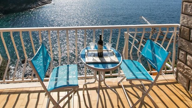 A balcony with two blue chairs and a table, overlooking a coastal sea with a clear view of the horizon. - Apartments Neve (Dubrovnik)