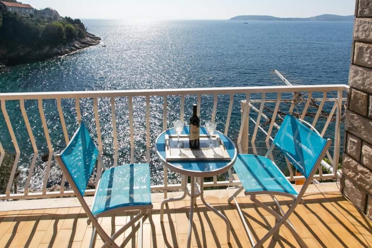 Varanda com duas cadeiras azuis e uma mesa, com vista para o mar costeiro e horizonte claro.