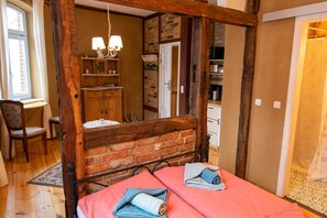 A bedroom with a four-poster bed, wooden beams, a brick wall, and a window with curtains.