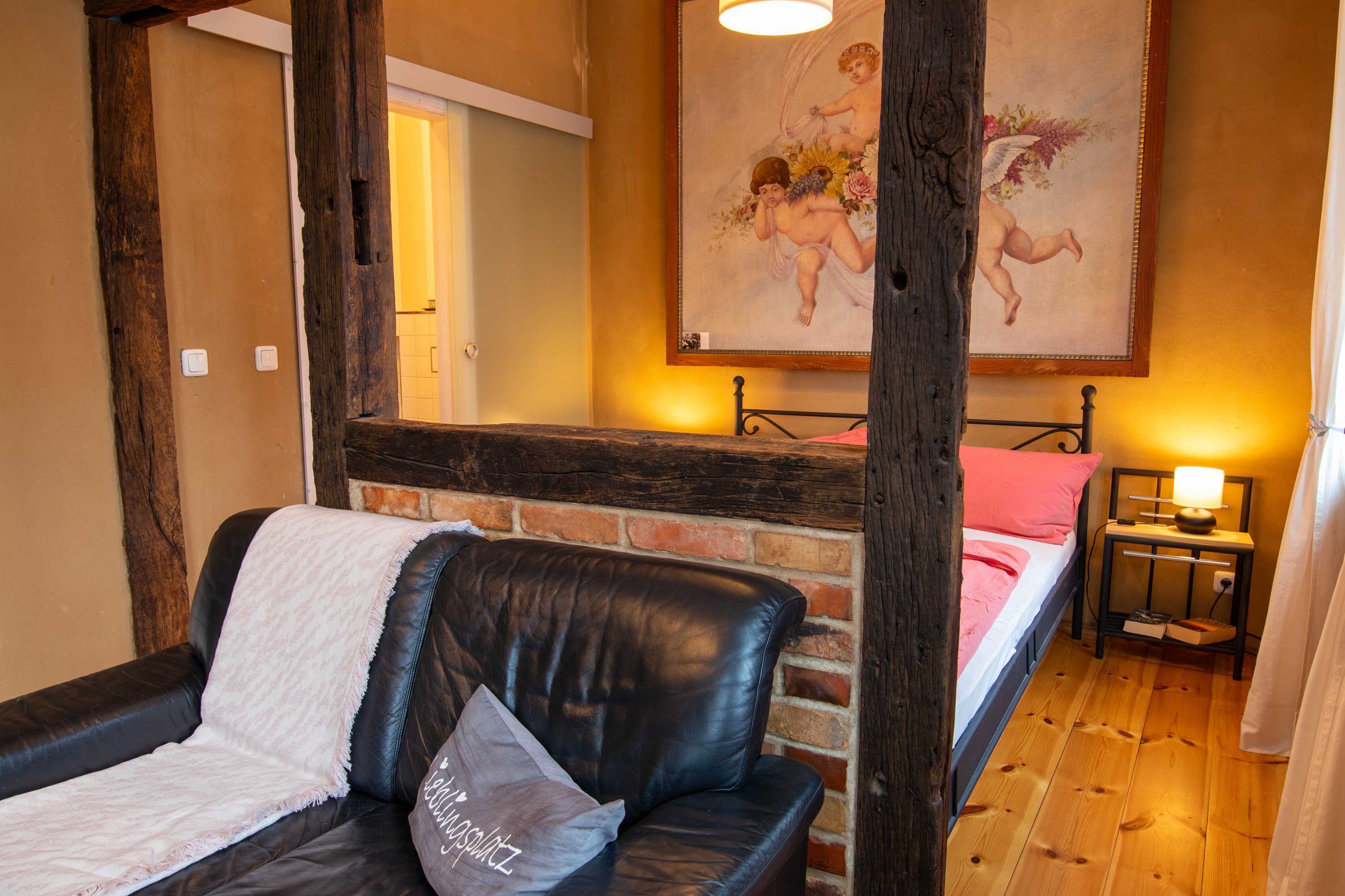 Une pièce chaleureuse avec un canapé en cuir, un lit doté d’une tête de lit en bois, une table de chevet avec une lampe et un tableau accroché au mur.